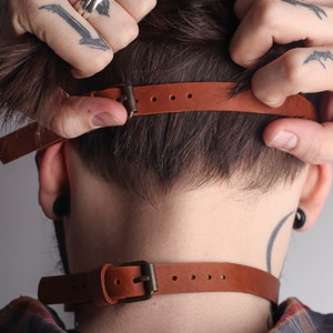 Może przedstawiać: Brązowy sk&oacute;rzany choker z klamrą. Choker jest regulowany i ma prosty design.