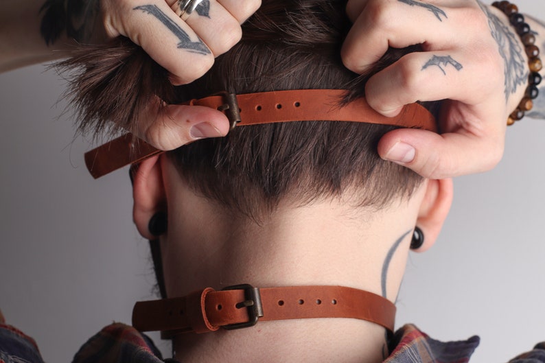 Może przedstawiać: Brązowy sk&oacute;rzany choker z klamrą. Choker jest regulowany i ma prosty design.