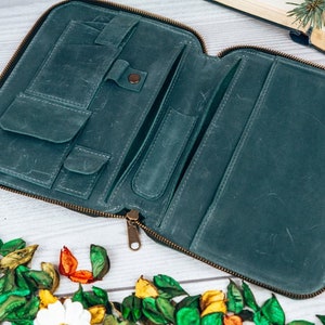 May include: A teal leather zippered wallet with multiple compartments and pockets. The wallet is open and lying on a white wooden surface.