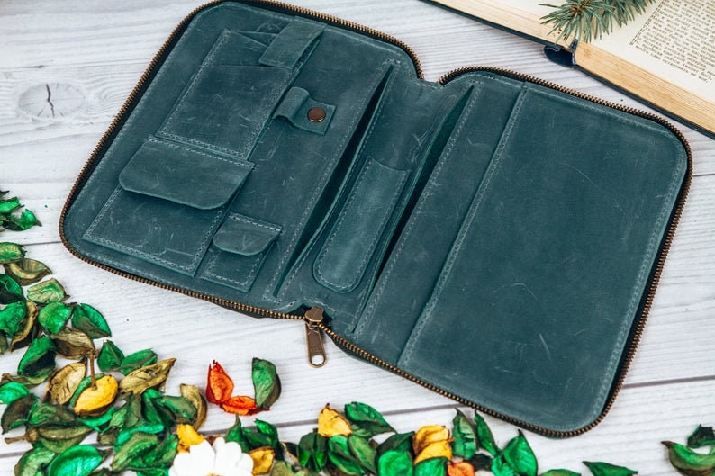 May include: A teal leather zippered wallet with multiple compartments and pockets. The wallet is open and lying on a white wooden surface.