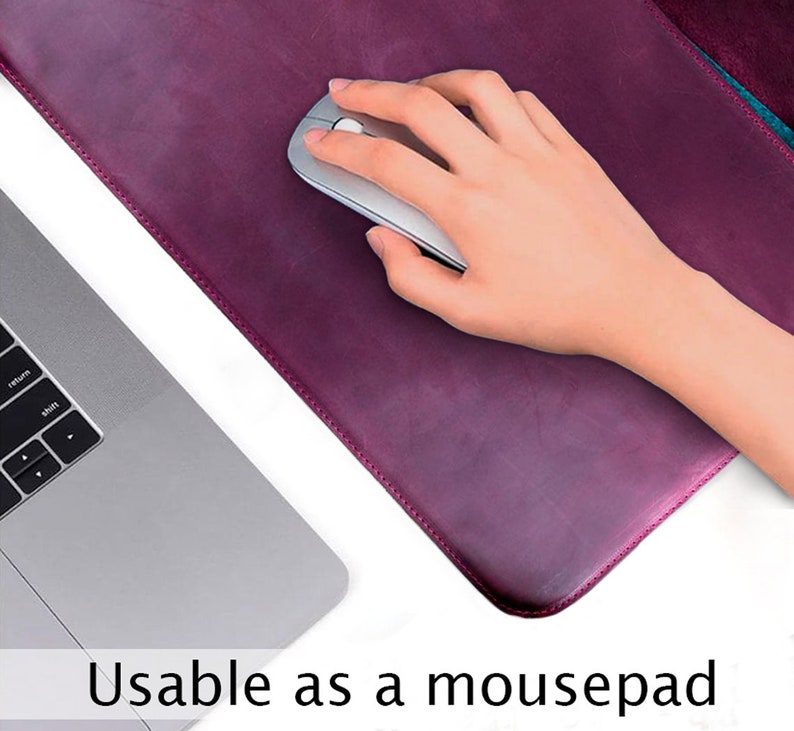 Puede incluir: Primer plano de una alfombrilla de rat&oacute;n de cuero burdeos con una mano usando un rat&oacute;n de ordenador plateado encima. El texto "Usable as a mousepad" est&aacute; en la parte inferior de la imagen.