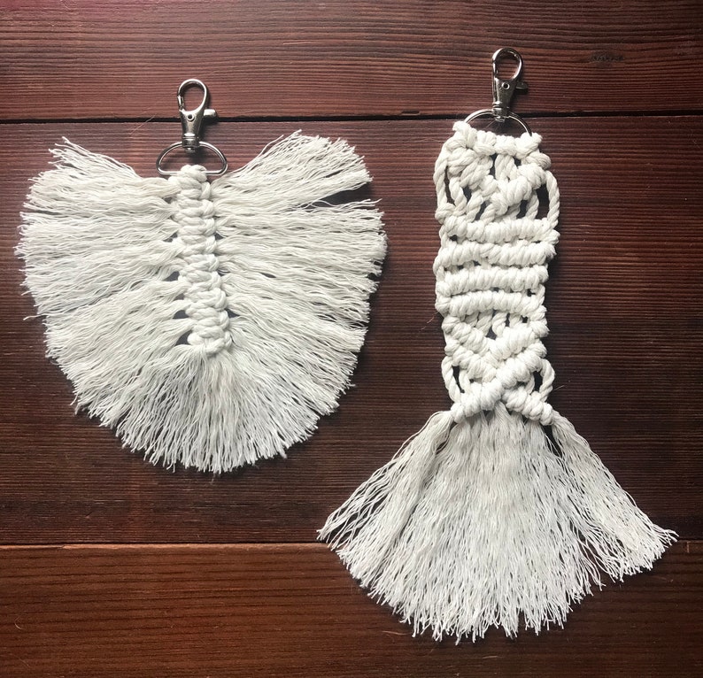 K&ouml;nnte beinhalten: Zwei wei&szlig;e Makramee-Schl&uuml;sselanh&auml;nger mit Fransen. Ein Schl&uuml;sselanh&auml;nger ist federf&ouml;rmig, der andere ist ein langes Rechteck.