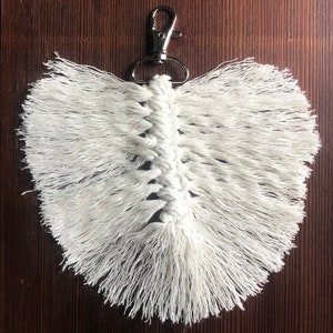 K&ouml;nnte beinhalten: Wei&szlig;er Makramee-Feder-Schl&uuml;sselanh&auml;nger mit einem silbernen Metallverschluss.