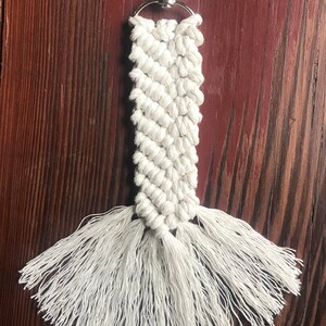 K&ouml;nnte beinhalten: Wei&szlig;er Makramee-Schl&uuml;sselanh&auml;nger mit einem silbernen Schl&uuml;sselring und langen wei&szlig;en Quasten.