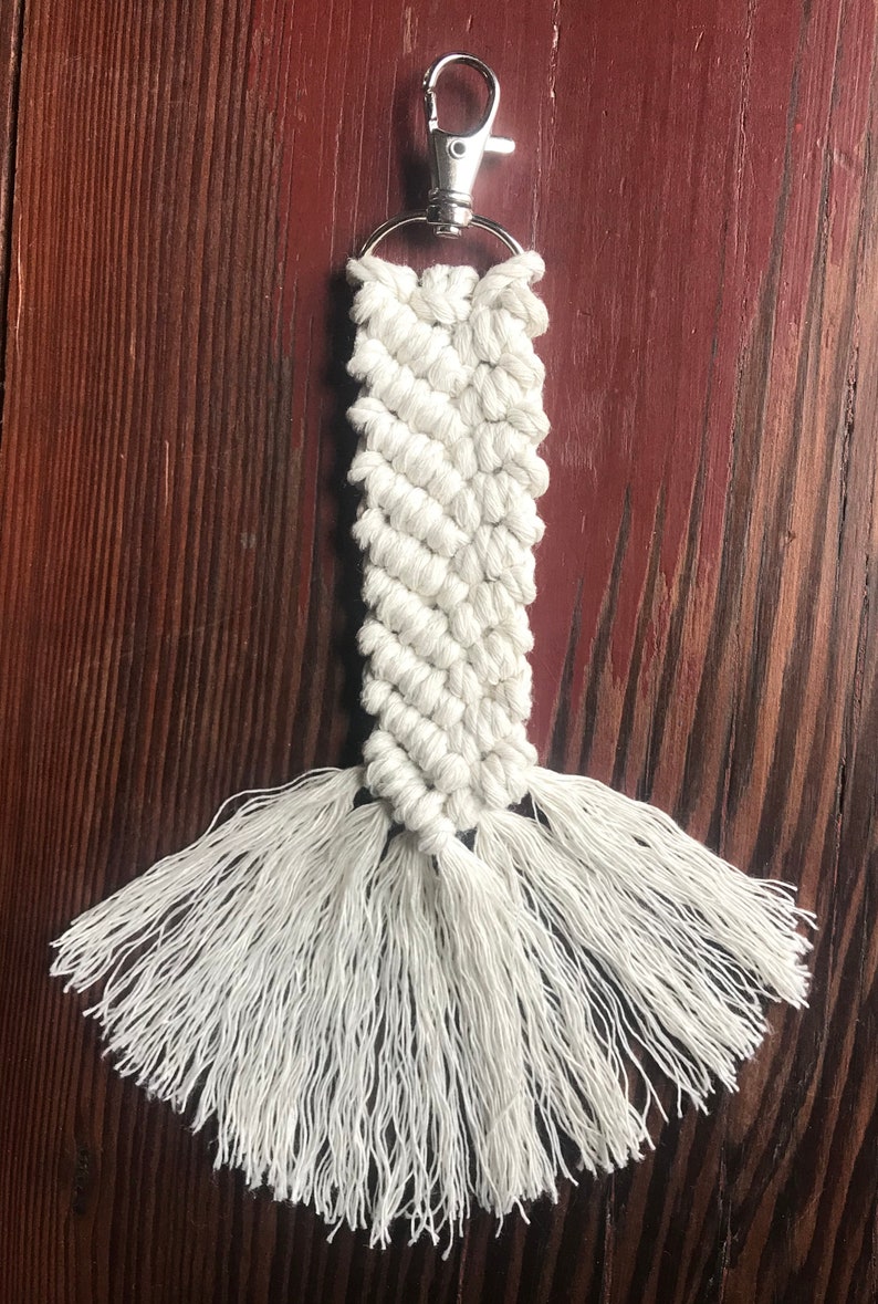 K&ouml;nnte beinhalten: Wei&szlig;er Makramee-Schl&uuml;sselanh&auml;nger mit einem silbernen Schl&uuml;sselring und langen wei&szlig;en Quasten.