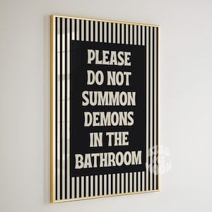 Könnte beinhalten: Gerahmter Kunstdruck mit goldenem Rahmen. Das Kunstwerk hat eine schwarze rechteckige Mitte mit weißem Text: „PLEASE DO NOT SUMMON DEMONS IN THE BATHROOM“. Der Hintergrund hat vertikale schwarz-weiße Streifen.
