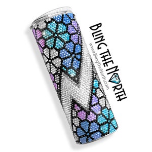 May include: A stainless steel tumbler with a colorful, geometric design featuring blue, purple, and white rhinestones. The tumbler is covered in rhinestones and has a black base. The text "BLING THE NORTH" and "www.BlingTheNorth.com" is printed on the side of the tumbler.