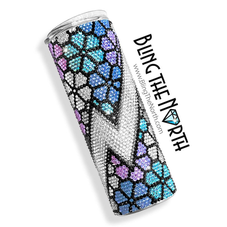 May include: A stainless steel tumbler with a colorful, geometric design featuring blue, purple, and white rhinestones. The tumbler is covered in rhinestones and has a black base. The text "BLING THE NORTH" and "www.BlingTheNorth.com" is printed on the side of the tumbler.