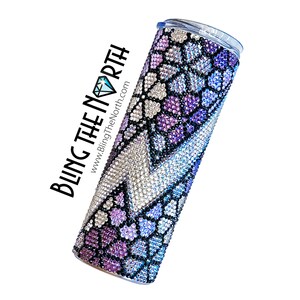 May include: A stainless steel tumbler with a purple, blue, and silver rhinestone design. The tumbler has a clear lid and is decorated with a snake skin pattern. The text "BLING THE NORTH" and "www.BlingTheNorth.com" is printed on the side of the tumbler.