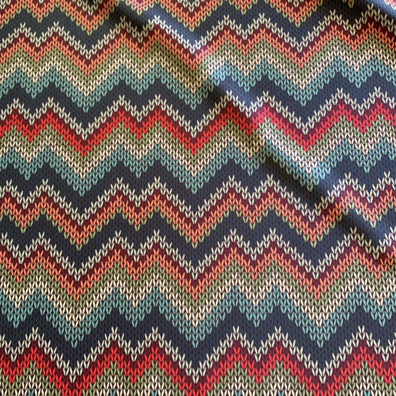Puede incluir: Una tela con un patr&oacute;n de chevron en tonos de rojo, naranja, verde, azul y blanco sobre un fondo azul oscuro.