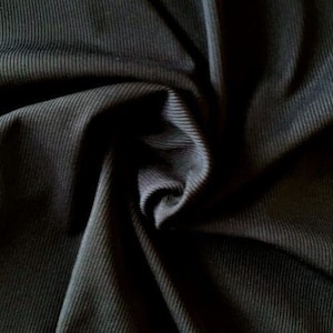 Puede incluir: Tela de canal&eacute; negra con una textura suave y el&aacute;stica. La tela est&aacute; doblada y drapeada, mostrando la textura y el drapeado del material.