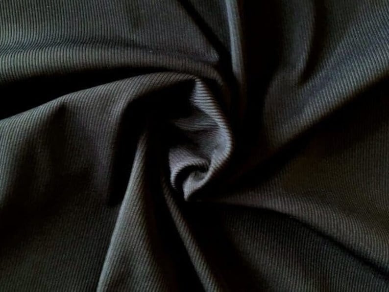 Puede incluir: Tela de canal&eacute; negra con una textura suave y el&aacute;stica. La tela est&aacute; doblada y drapeada, mostrando la textura y el drapeado del material.