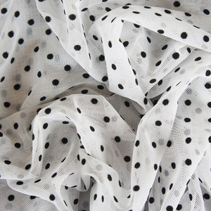 May include: White sheer fabric with black polka dots. The fabric is gathered and draped, showing the texture of the material.