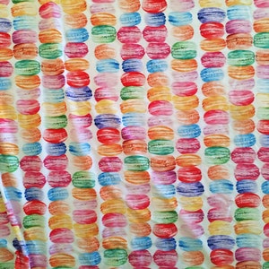 Puede incluir: Una tela blanca con un patr&oacute;n repetido de macarons coloridos. Los macarons est&aacute;n dispuestos en filas y est&aacute;n pintados en tonos de rosa, azul, verde, amarillo y naranja.