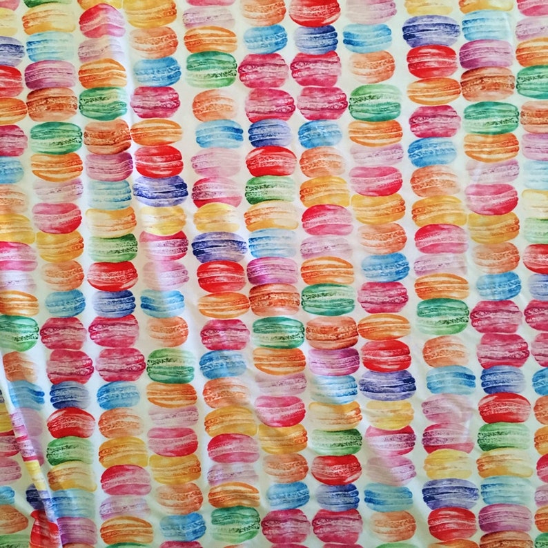 Puede incluir: Una tela blanca con un patr&oacute;n repetido de macarons coloridos. Los macarons est&aacute;n dispuestos en filas y est&aacute;n pintados en tonos de rosa, azul, verde, amarillo y naranja.