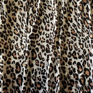 May include: Close-up of a fabric with a leopard print pattern. The fabric is white with brown and pink spots.