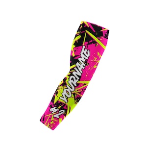 May include: A pink and black arm sleeve with a neon yellow splatter design. The text "YOURNAME" is printed in white, with the number "2" and a hashtag symbol. The sleeve is designed to fit the arm.