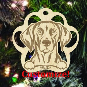 May include: A wooden paw print ornament with a dog's head peeking out. The dog is brown and white and has a black nose. The ornament has the name "HEIDI" written on it. Customize! is written below the name.