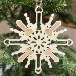 May include: A wooden snowflake ornament with a unique design featuring multiple guitar shapes. The ornament is light brown and has a string for hanging.