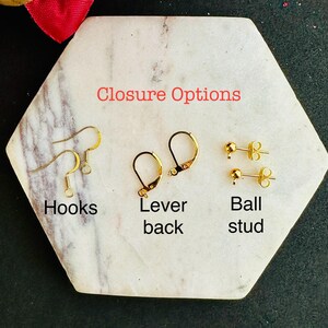 May include: Three types of gold-toned earring findings labeled Closure Options: a pair of wire hooks labeled Hooks, a pair of hinged lever back findings labeled Lever back, and a pair of ball stud posts labeled Ball stud.