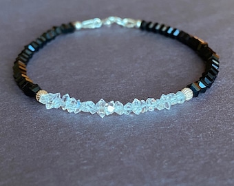 May include: A delicate bracelet with a two-tone design. One half of the bracelet is made of black beads, while the other half is made of clear, faceted beads. The bracelet is secured with a silver clasp.