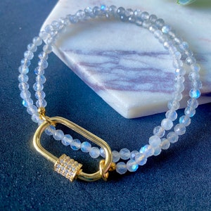 May include: A double-strand bracelet made with iridescent white beads and a gold clasp with clear rhinestones.