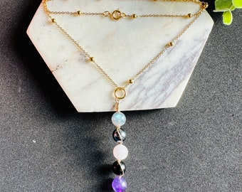 May include: A gold chain necklace with a pendant made of five gemstone beads. The beads are a light blue, black, pink, black, and purple.