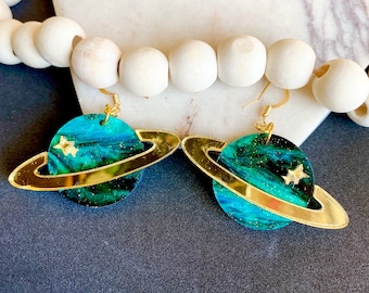May include: A pair of gold and green planet earrings with a gold ring around each planet. The planets have a dark green and blue marbled design with gold glitter and gold stars.