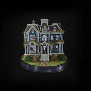 Peut inclure: Modèle miniature d'une maison bleue à deux étages avec des fenêtres barricadées et des vignes envahissantes. La maison est sur une petite base circulaire avec de l'herbe verte et de la terre brune.