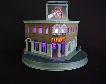 May include: A miniature model of a brick building with a sign that reads "Flynn's" and a billboard above that says "Space Paranoids". The building has windows and a door, and the sign is lit up with purple lights.