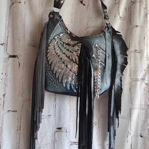 May include: A black leather handbag with silver sequin wings and black fringe. The bag has a zip closure and a chain strap.