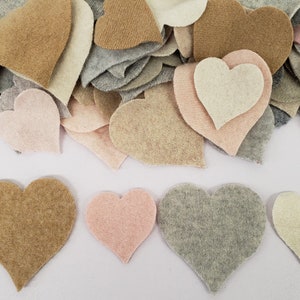 Peut inclure: Une collection de découpes en forme de cœur en feutrine dans diverses nuances de gris, beige, brun clair et rose pâle. Les cœurs sont éparpillés en un tas sur le dessus, avec quatre cœurs individuels disposés en rangée au bas du cadre.