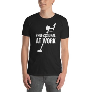 Puede incluir: Camiseta negra con un gráfico blanco de un detector de metales y el texto "PROFESSIONAL AT WORK". El diseño tiene un aspecto envejecido y vintage. La camiseta está hecha de un material suave.