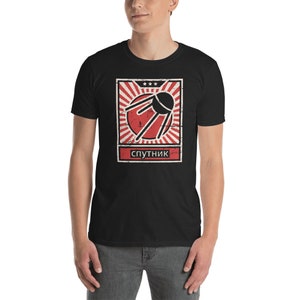 Op de afbeelding: Een zwart T-shirt met een rode, witte en blauwe afbeelding van een satelliet met de tekst "SPUTNIK" in wit.