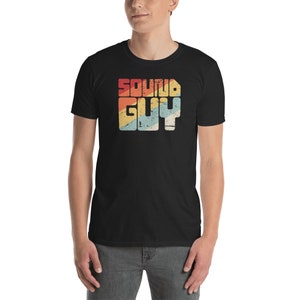 Może przedstawiać: Czarny t-shirt z grafiką w stylu vintage, na którym widnieje napis "SOUND GUY" w kolorowych literach.