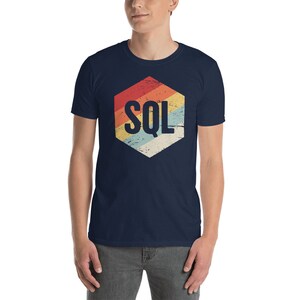 May include: A navy blue t-shirt with a retro-style hexagon design featuring the text "SQL" in white. The hexagon has a faded, vintage look with stripes of red, orange, yellow, green, and blue.