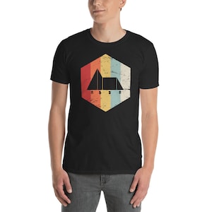 Puede incluir: Una camiseta negra con un gráfico retro de un triángulo con las letras A, B, S y A en su interior. El gráfico está en una forma hexagonal con un esquema de color arcoíris descolorido.