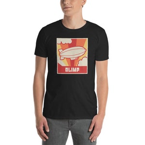 May include: A black t-shirt with a retro-style graphic of a blimp flying in the sky. The graphic is in red, orange, and yellow colors with the word "BLIMP" printed in white below the blimp.