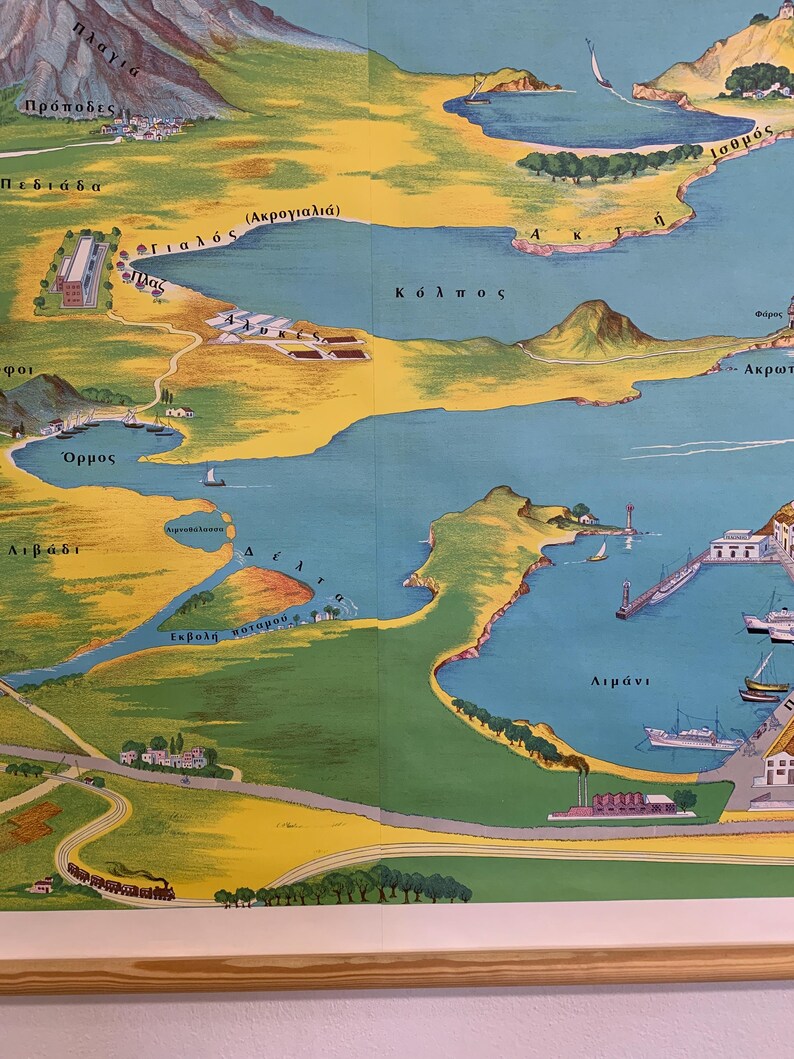 May include: A vintage map illustration featuring a coastal landscape with blue waters, yellow land, and green vegetation. The map includes Greek text, depicting bays, towns, and geographical features. The map is framed in a light brown wooden frame.