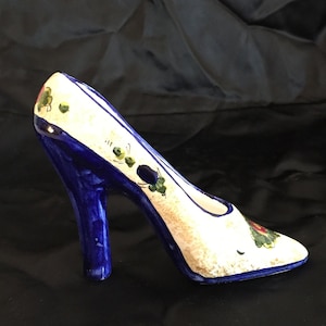 May include: A white ceramic high-heeled shoe with blue and green floral designs. The shoe is a decorative object.