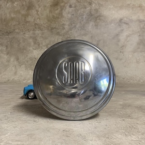 Könnte beinhalten: Eine silberne Radkappe mit dem Wort "SAAB" in der Mitte geprägt.