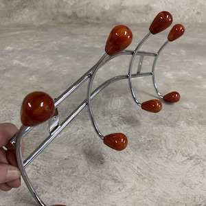 Op de afbeelding: Een chromen kapstok met zes haken. De haken zijn voorzien van ronde, oranje-bruine plastic knoppen.