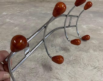 May include: Chrome coat rack with six hooks. The hooks are topped with round, orange-brown plastic knobs.