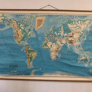 May include: A large vintage wall map of the world printed on paper with wooden dowels at the top and bottom for hanging. The map features blue oceans and tan and green landmasses with Greek text labels throughout and a legend in the corner.