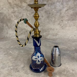 May include: A blue glass hookah with silver floral designs and a gold metal stem. The hookah includes a silver metal bowl, a small wooden bowl, and a black and gold hose.