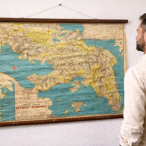 May include: A vintage map of a coastal region, possibly Greece, in teal and beige tones. The map is mounted on wooden rods and suspended by a string. It displays detailed geographical information, including roads and place names, and is a decorative item.