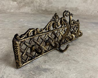 May include: A gold metal wall mounted coat rack with a decorative lattice design and three hooks.