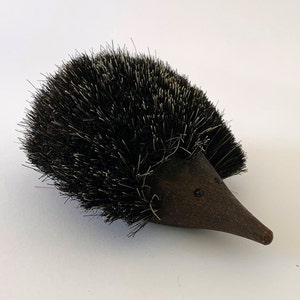 以下が含まれることがあります： 黒い目をした茶色の陶器のハリネズミ。体は黒いブラシでできています。