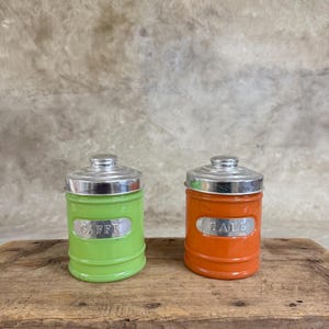 Può includere: Due barattoli di vetro vintage con coperchi argentati. Il barattolo verde dice "CAFFE" e il barattolo arancione dice "SALE".