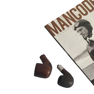 May include: Two wooden pipes, one with a silver band, on a white surface. A magazine with the title "MANCODE" is in the background.